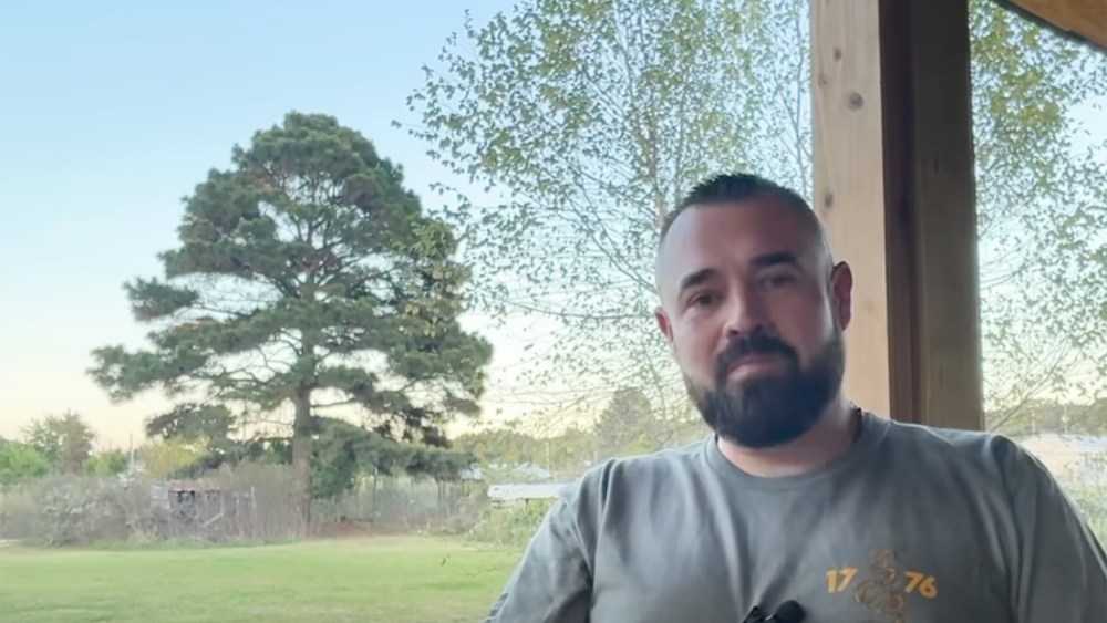 Aaron Spencer sits at a porch as he speaks. Turkeys can be seen in the background.