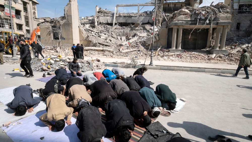 Men put their faces on the ground as they pray outside the ruins of a building.