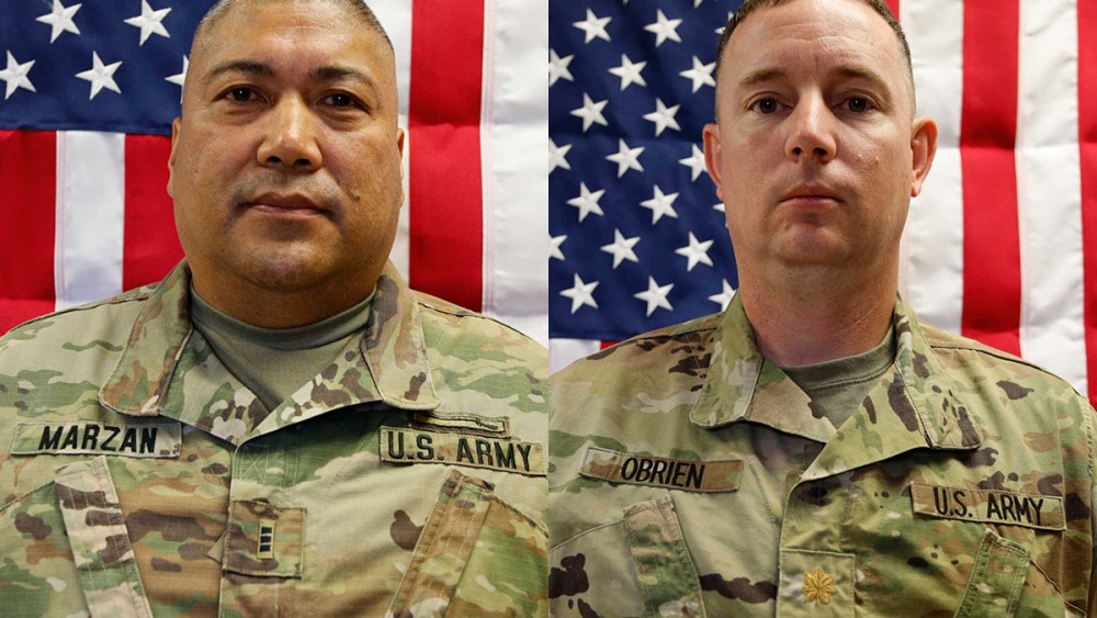 Two people in army uniforms in front of American flags.