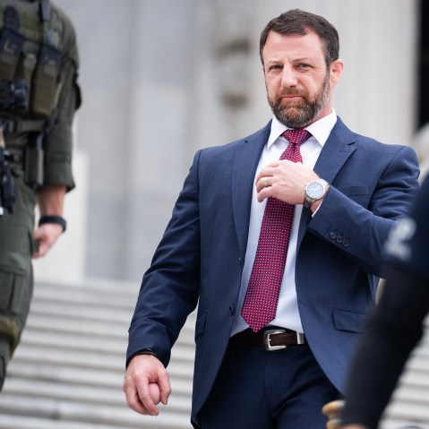 While Se. Mullin walks down the stairs there are two security personnel around him, one in front of him and one behind him.