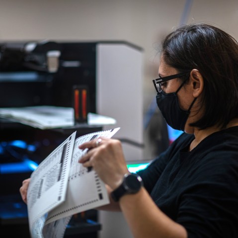 A person wearing a mask holds ballots.
