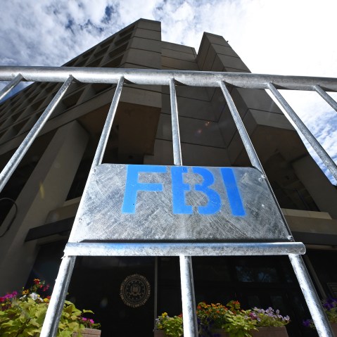 A metal fence with a sign that says "FBI" in blue letters is illuminated with flash in front of the FBI headquarters.