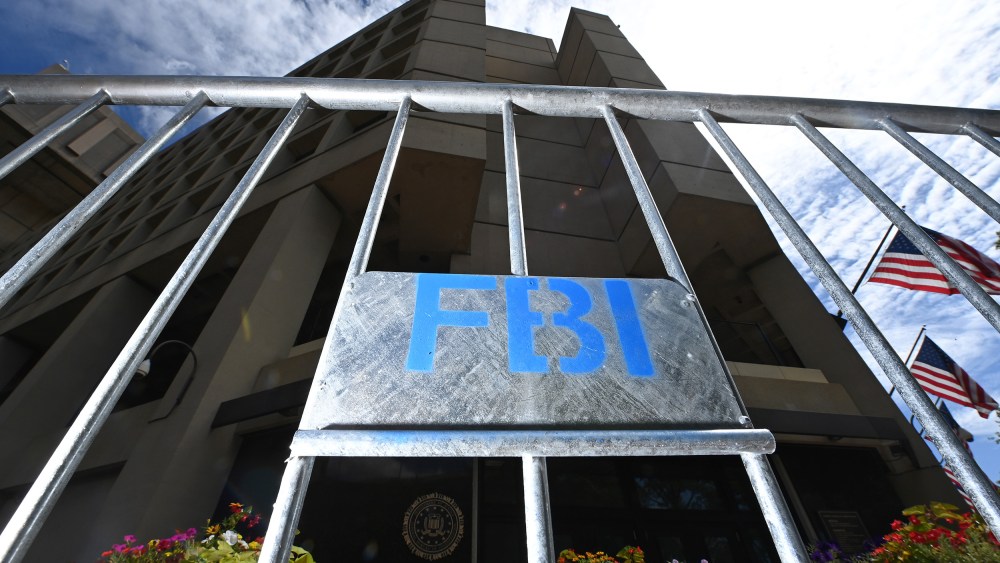A metal fence with a sign that says "FBI" in blue letters is illuminated with flash in front of the FBI headquarters.