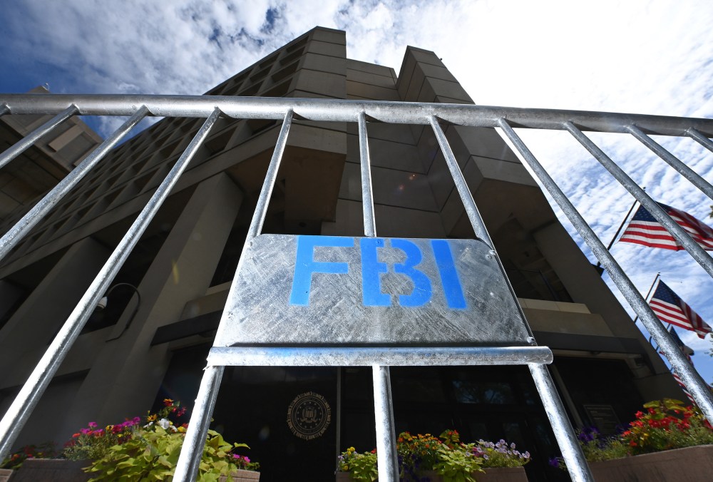 A metal fence with a sign that says "FBI" in blue letters is illuminated with flash in front of the FBI headquarters.
