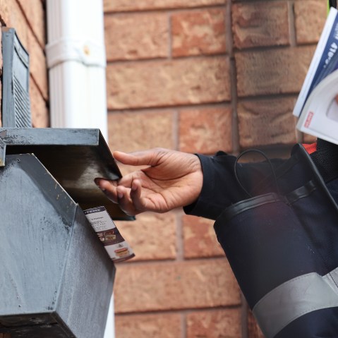 A Post carrier works handing out flyers with mail on his route.