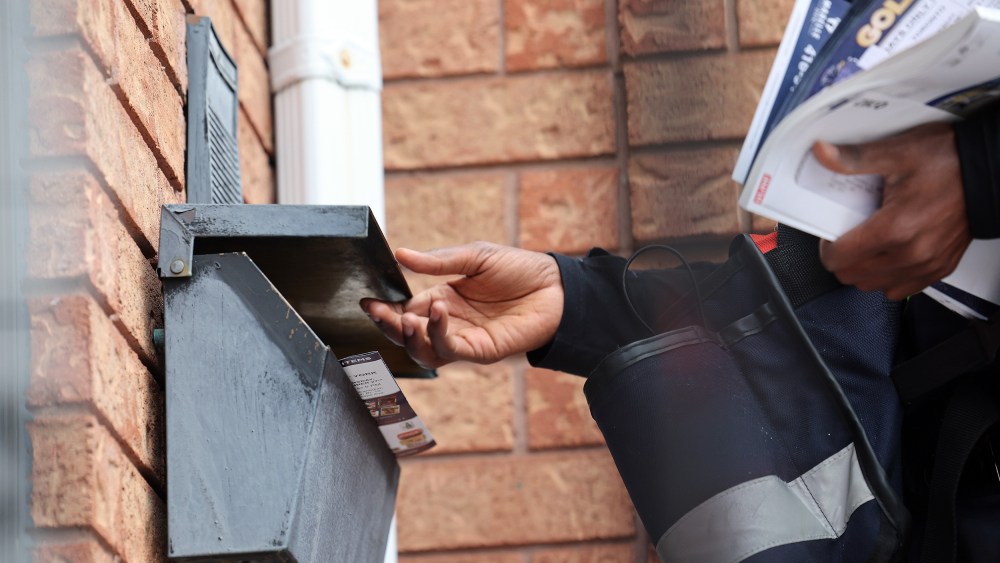 A Post carrier works handing out flyers with mail on his route.