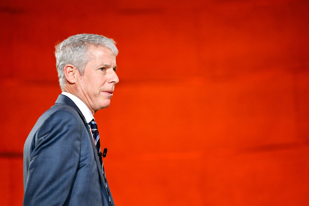 Chris Wrights walks towards right side of the frame in front of a red background.