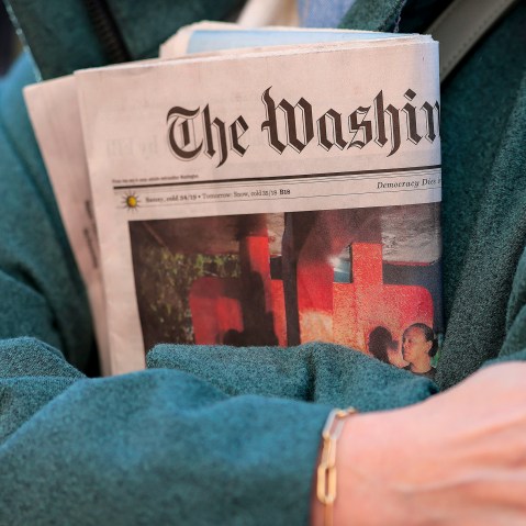 In this close-up shot of crossed arms, a woman holds a copy of The Washington Post tightly.